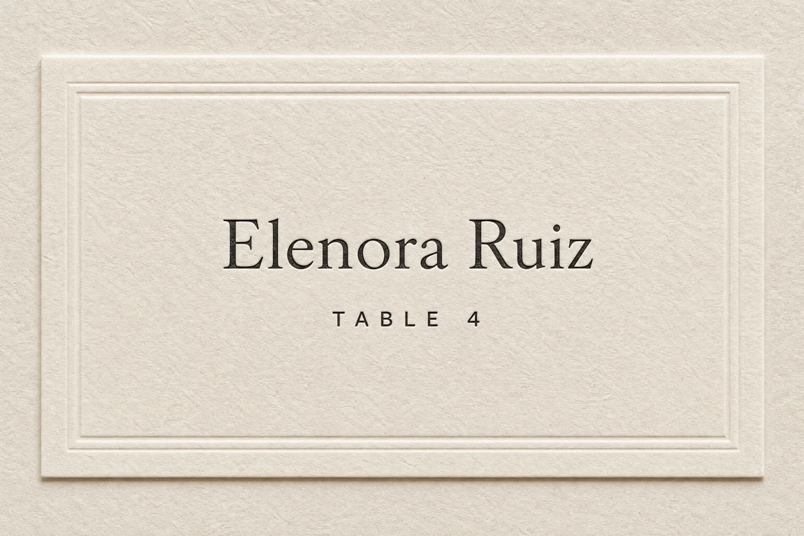 A wedding place card printed with a guest name and table number, lying on embossed cream paper